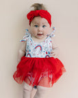 Baby wearing a red dress with a colorful pattern on a beige background