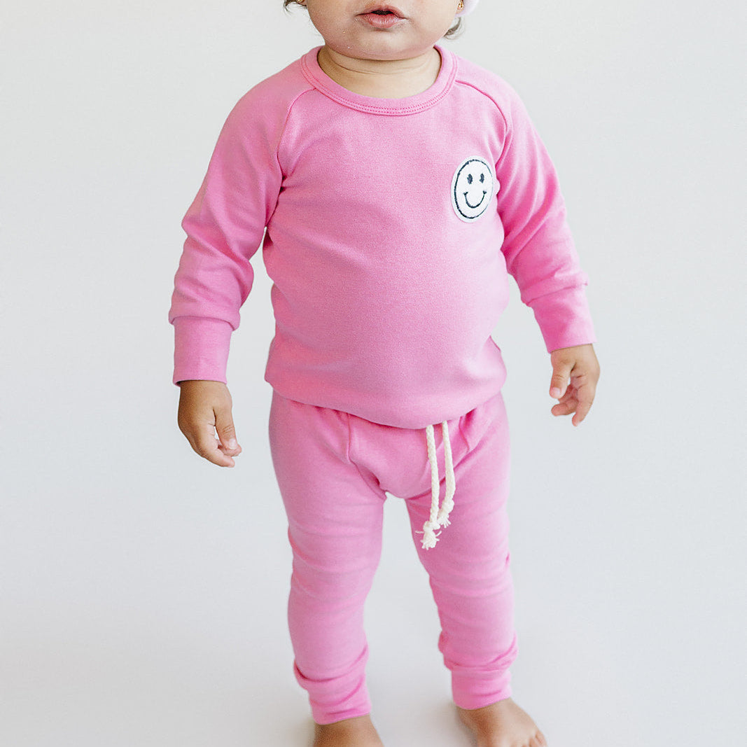 Baby wearing a pink outfit with smiley face design on a white background