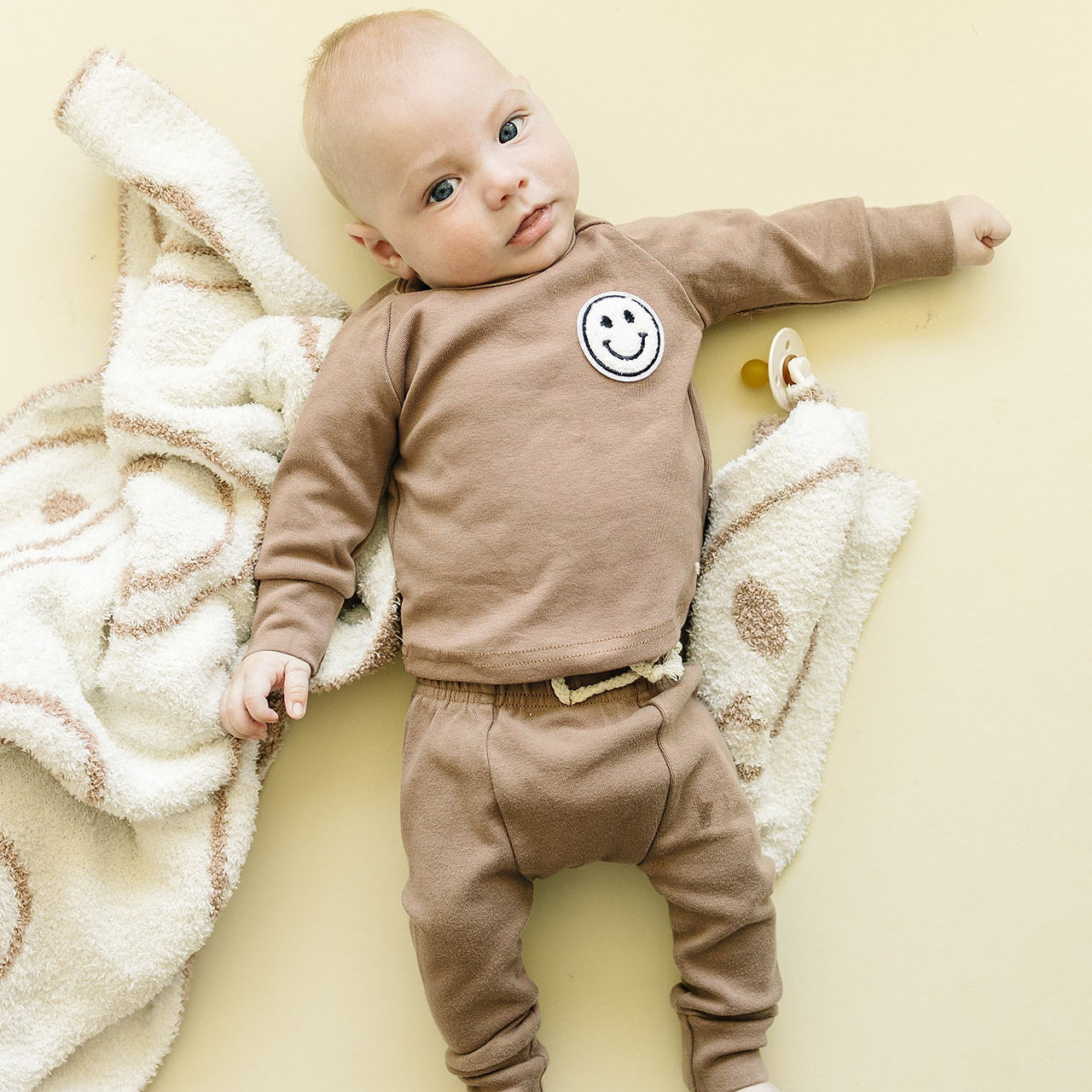 Baby wearing a brown outfit with a smiley face on a yellow background