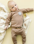 Baby wearing a brown outfit with a smiley face on a yellow background