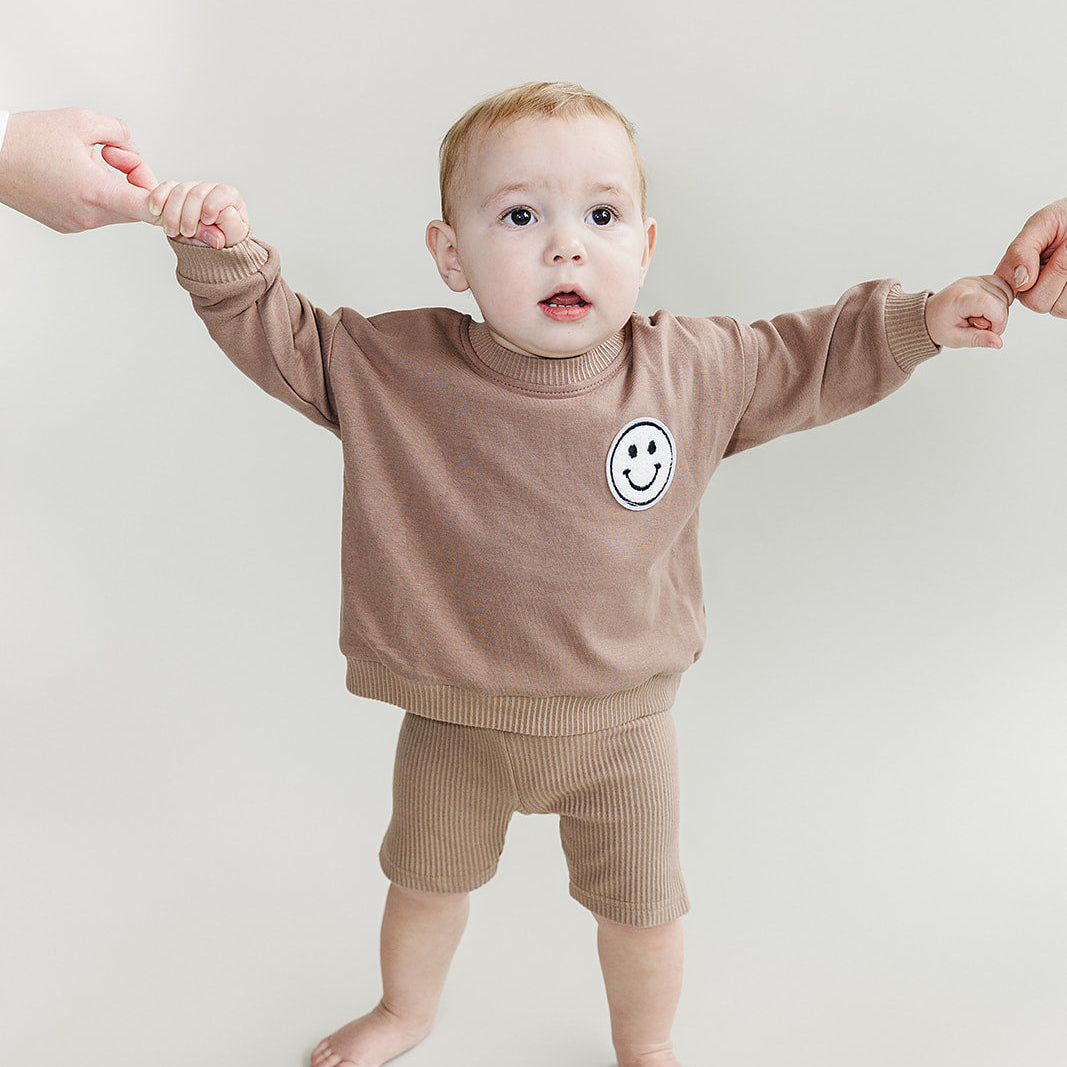Child wearing a brown sweatshirt with a smiley face design on a plain background