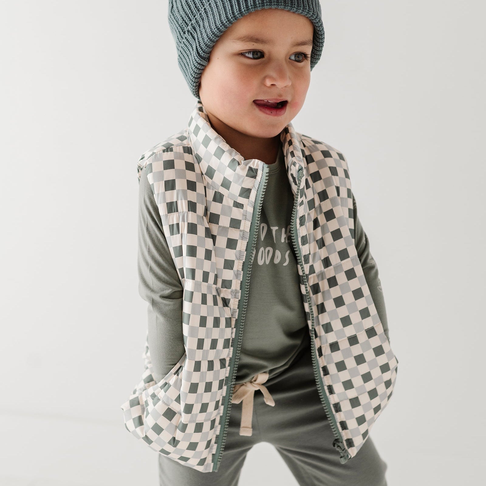Child wearing a checkered vest, striped shirt, and gray pants on a white background