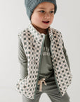 Child wearing a checkered vest, striped shirt, and gray pants on a white background