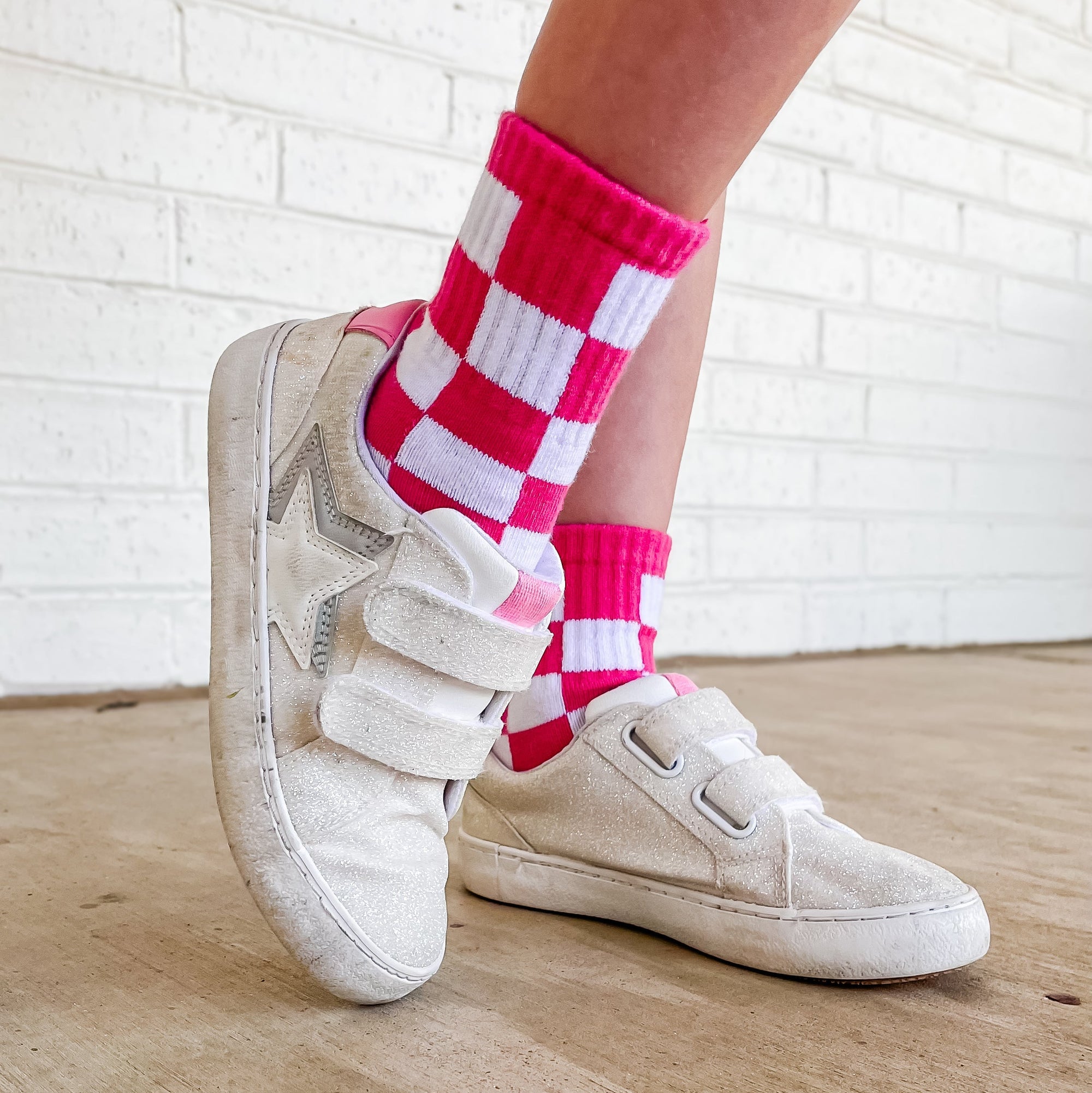 White sneakers with red and white checkered socks on a wooden floor.