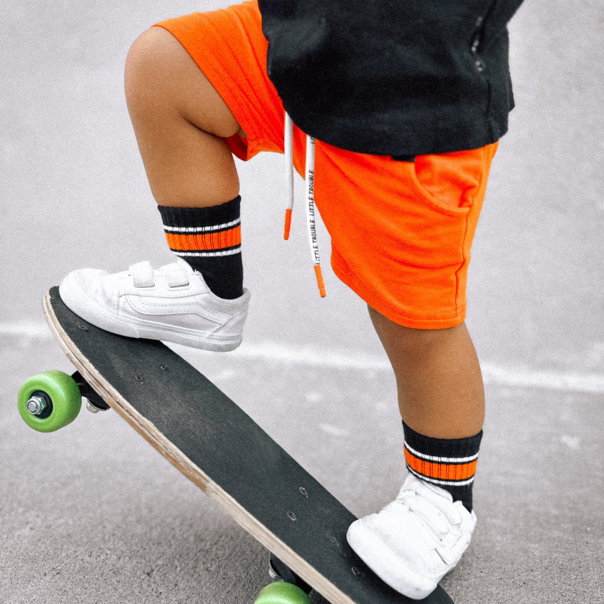Person wearing orange shorts and white sneakers with green wheels on a skateboard.