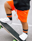 Person wearing orange shorts and white sneakers with green wheels on a skateboard.