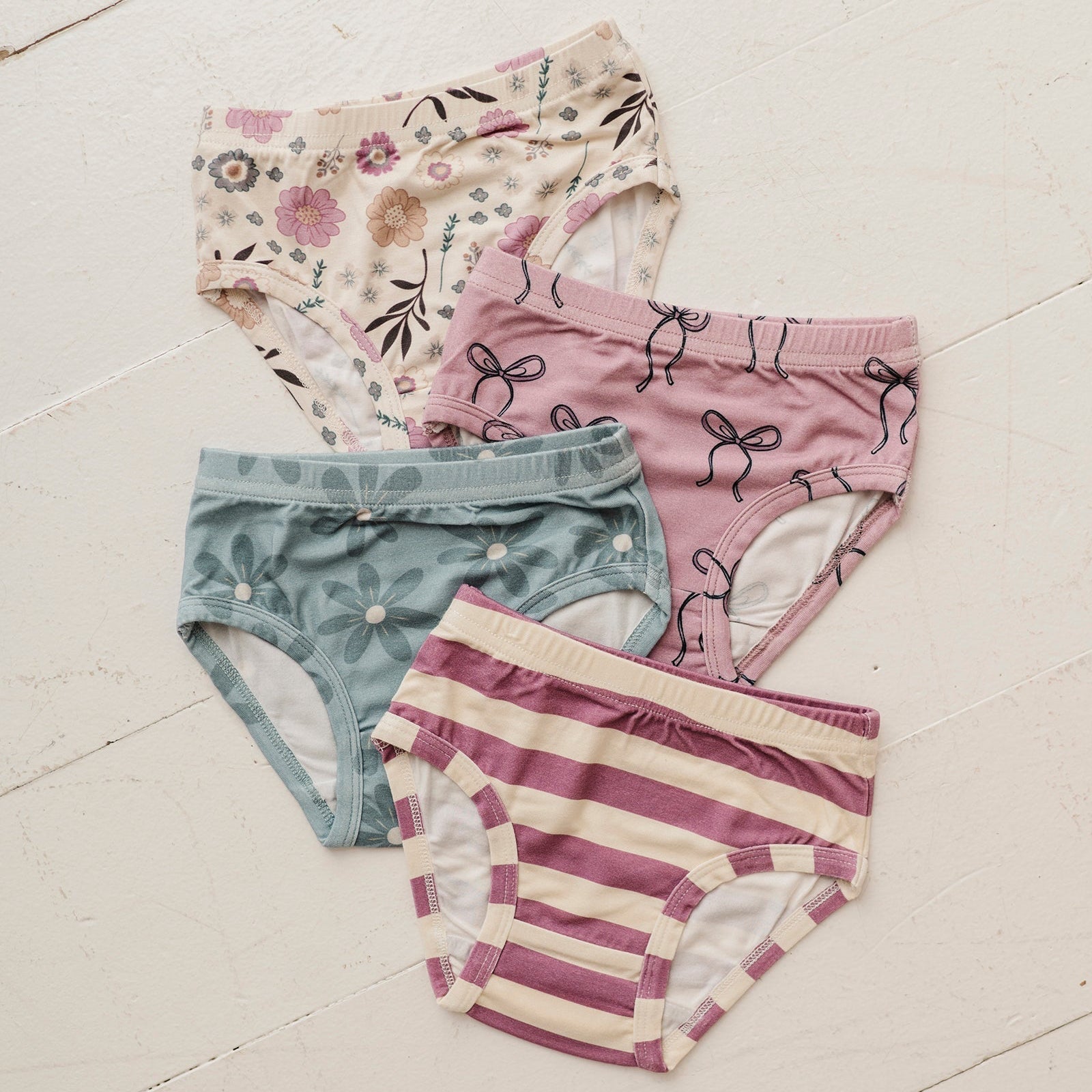 Four pairs of women's underwear with floral, striped, and other patterns on a light wooden floor.