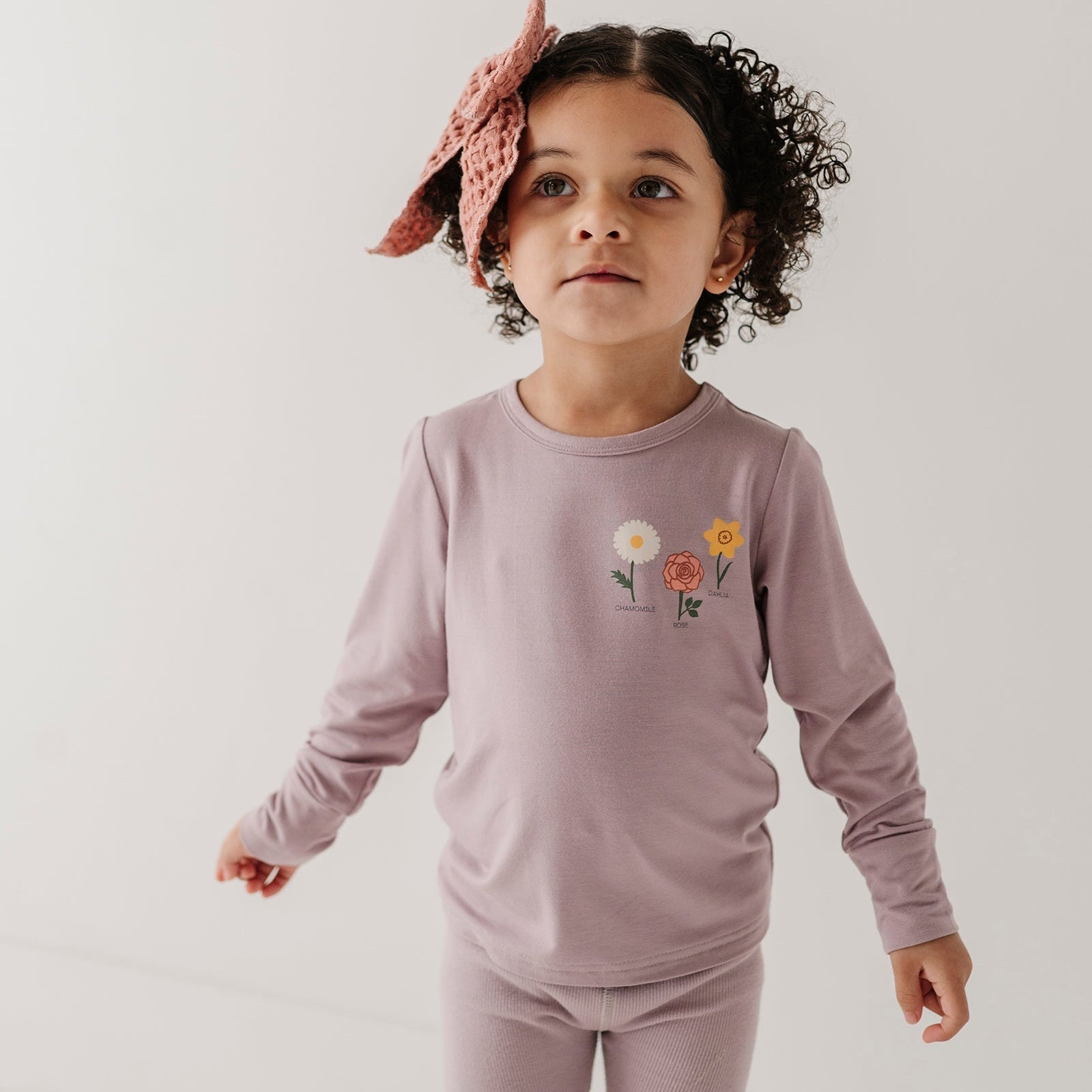 Child wearing a matching outfit with a floral headband on a plain background