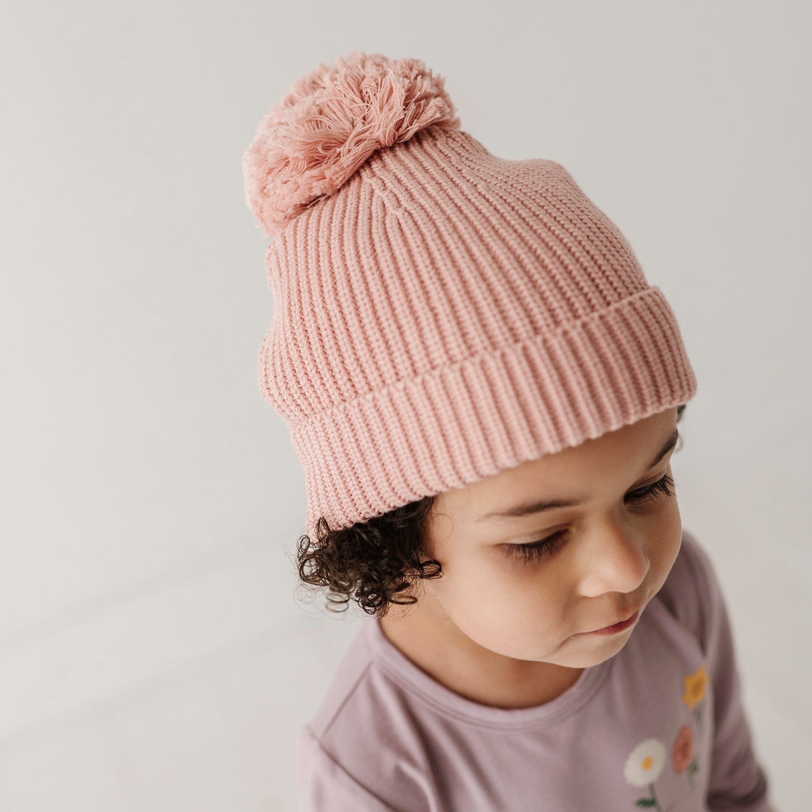 Child wearing a pink knit beanie with a pom-pom on a plain background