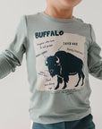 Child wearing a gray long-sleeve shirt with a graphic of a buffalo and text.