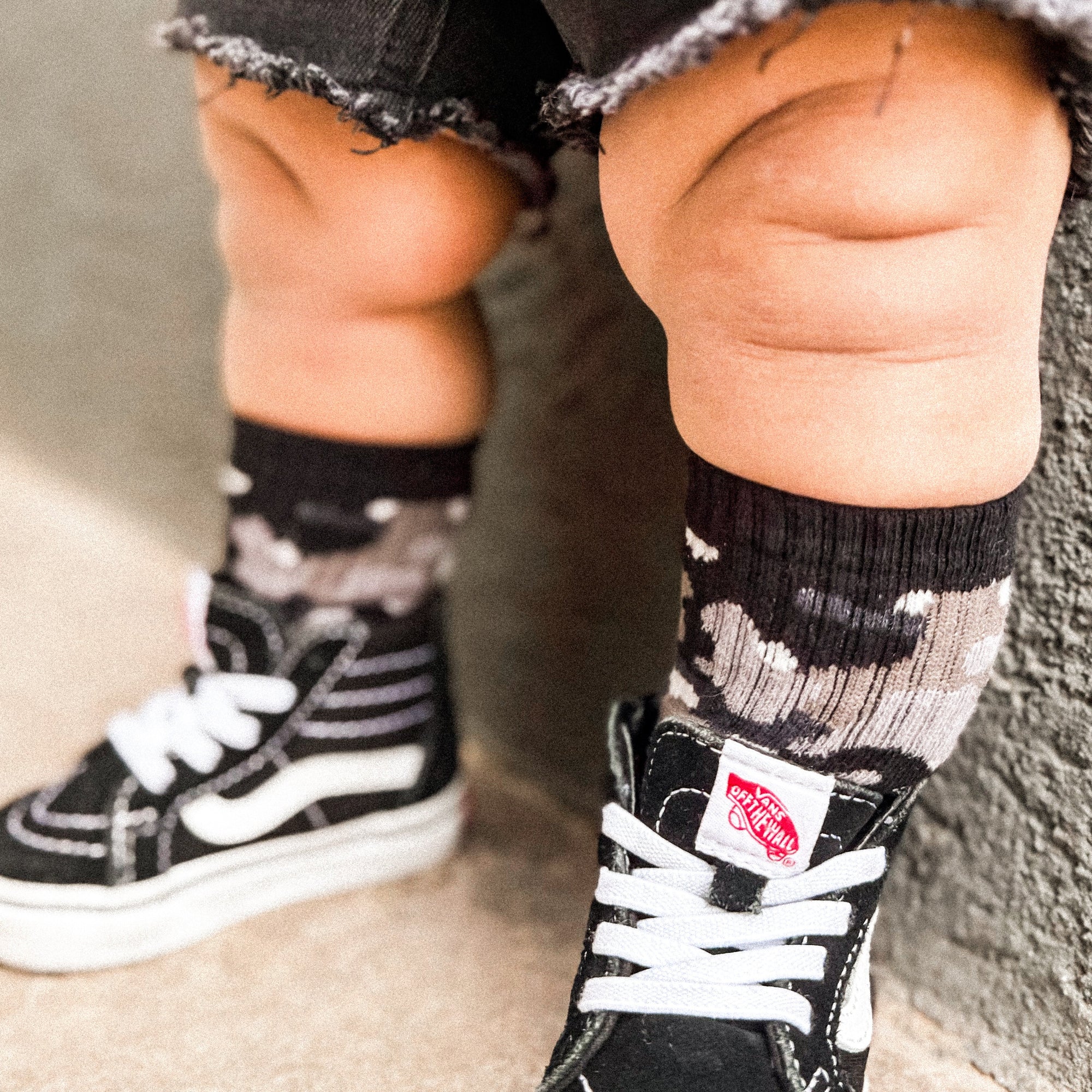 Child wearing black and white Vans shoes with socks, standing on a carpeted floor.