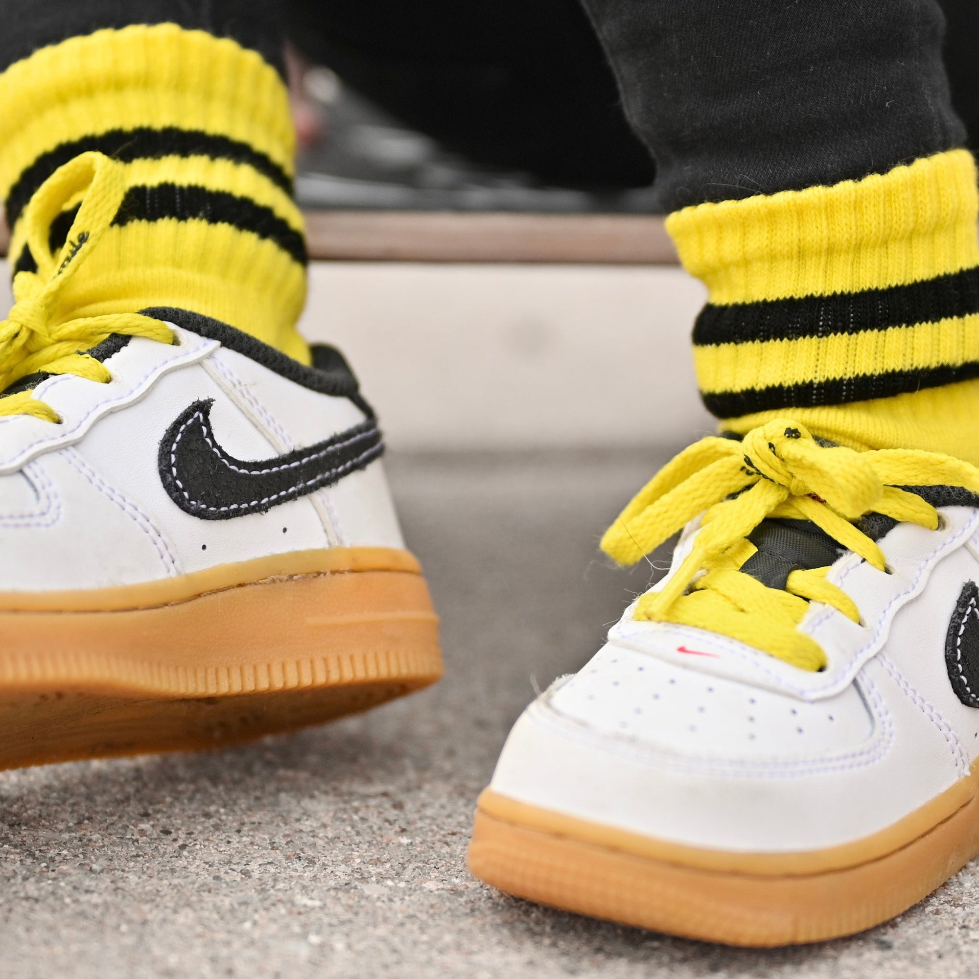 White sneakers with black swoosh logo and yellow accents worn with yellow socks.