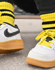 White sneakers with black swoosh logo and yellow accents worn with yellow socks.