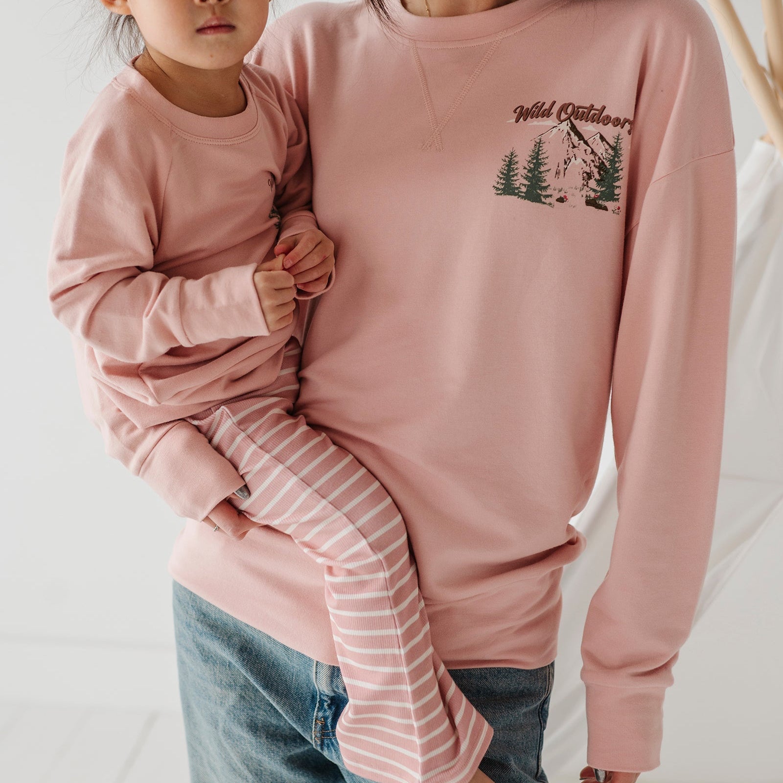 Woman holding a child both wearing pink sweatshirts with nature-themed designs.