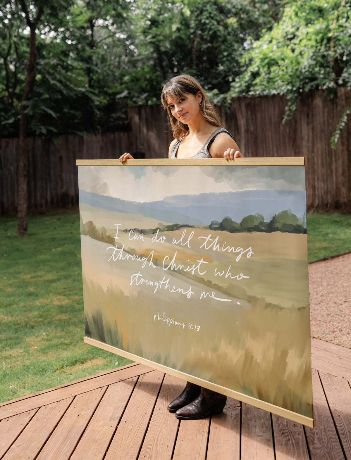 Angled view of the I Can Do All Things Through Christ canvas wall banner held outdoors on a wooden deck