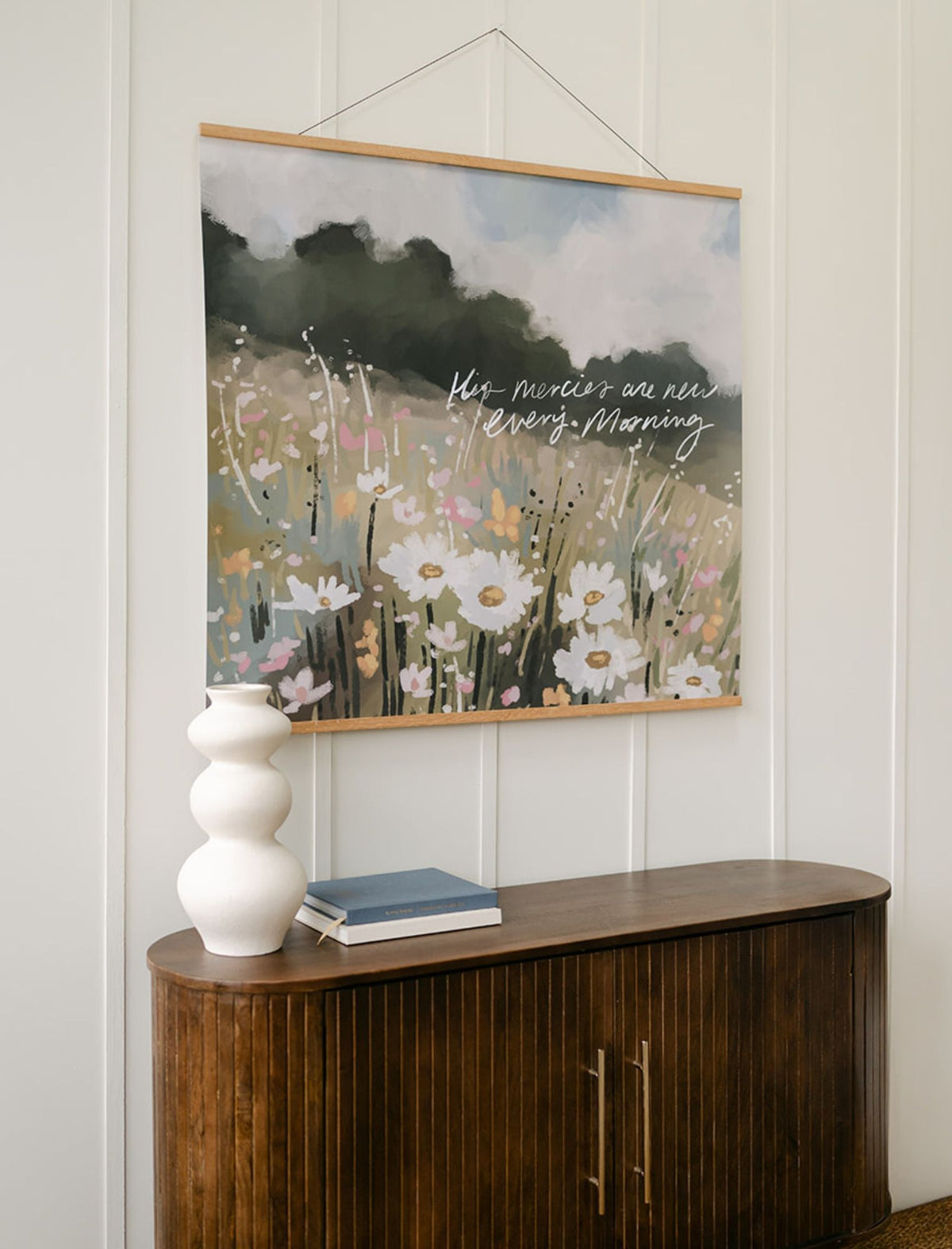 Angled view of the floral scripture wall art with wood banner hangers, styled above a cabinet beside a white vase