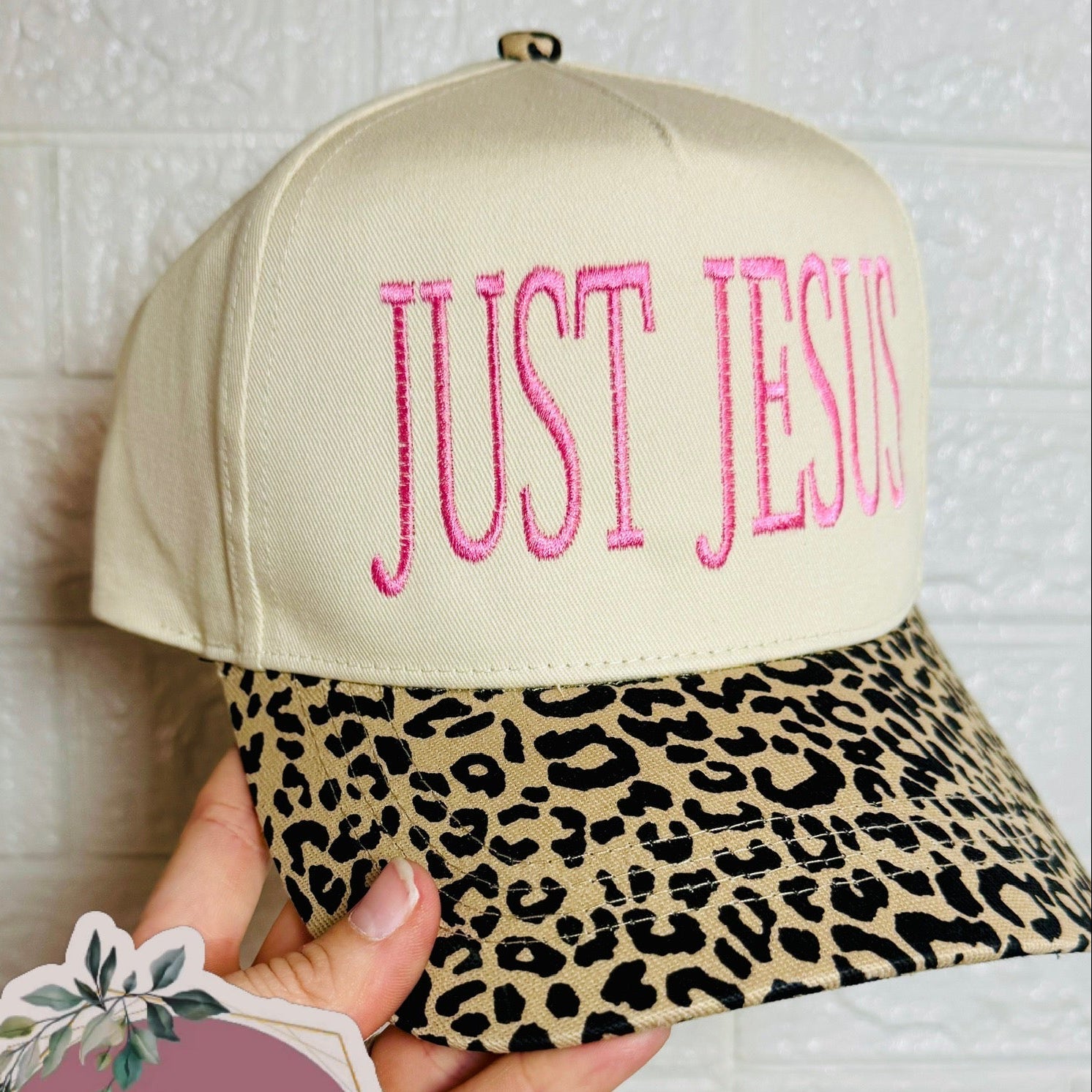 Beige cap with pink 'JUST JESUS' text and leopard print brim, held by a hand with GG&amp;CO. sticker.