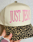 Beige cap with pink 'JUST JESUS' text and leopard print brim, held by a hand with GG&CO. sticker.