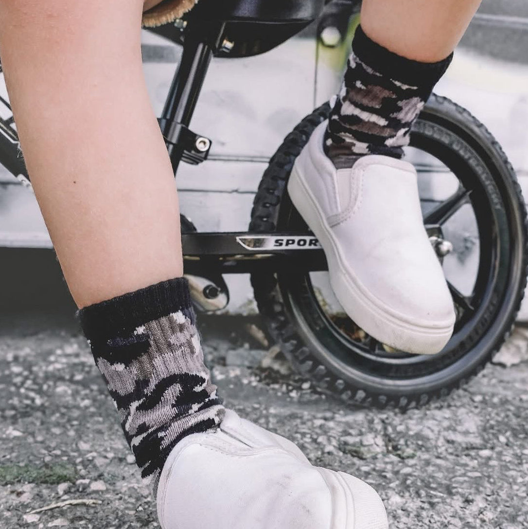 Person wearing white sneakers and patterned socks on a bicycle.