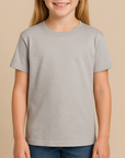Young girl wearing a light grey Gildan 8000B Youth DryBlend T-Shirt on a neutral beige studio background — soft cotton-poly tee ideal for custom printing by Lumiere Vive.