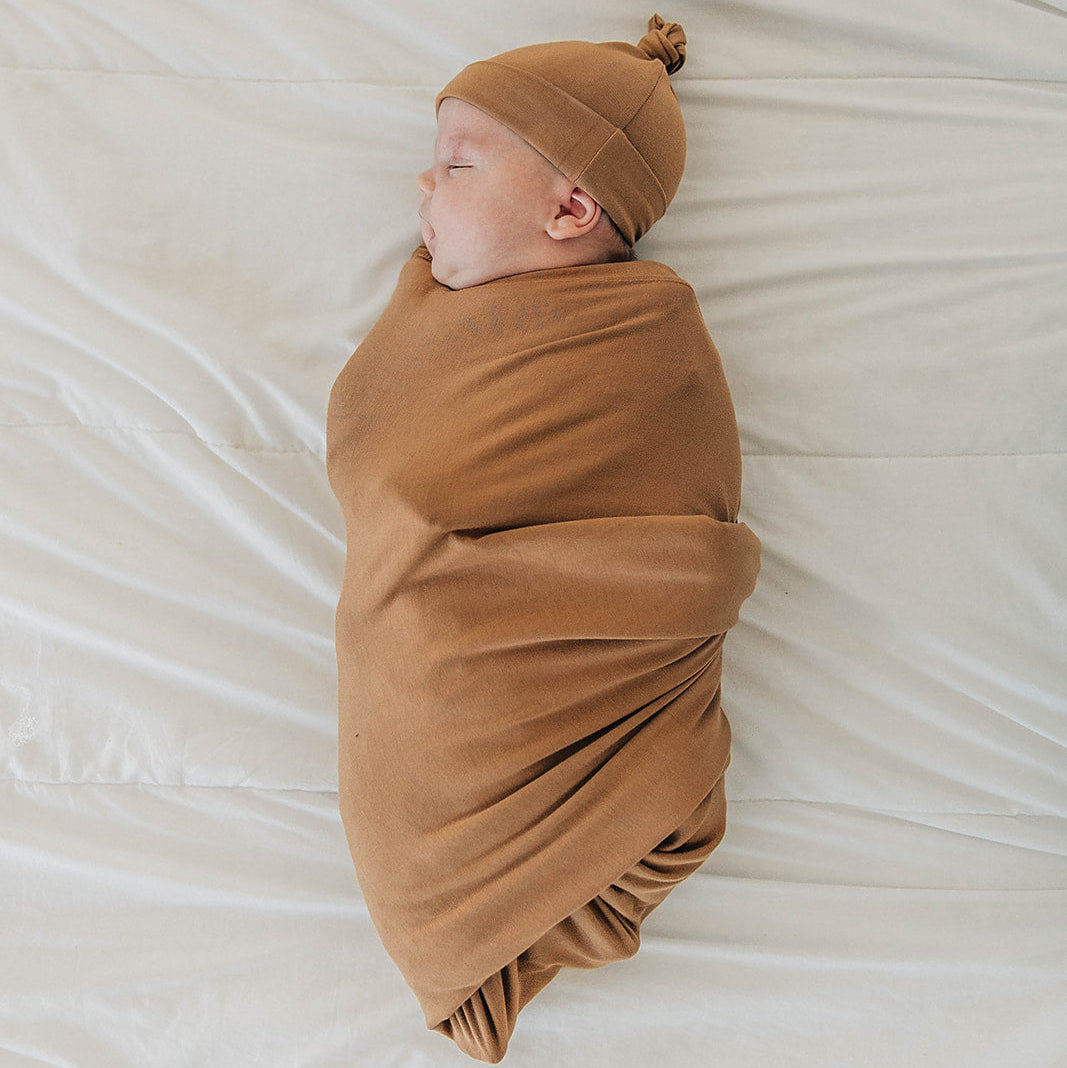 Newborn baby swaddled in a brown blanket and hat on a white background