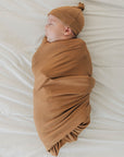 Newborn baby swaddled in a brown blanket and hat on a white background