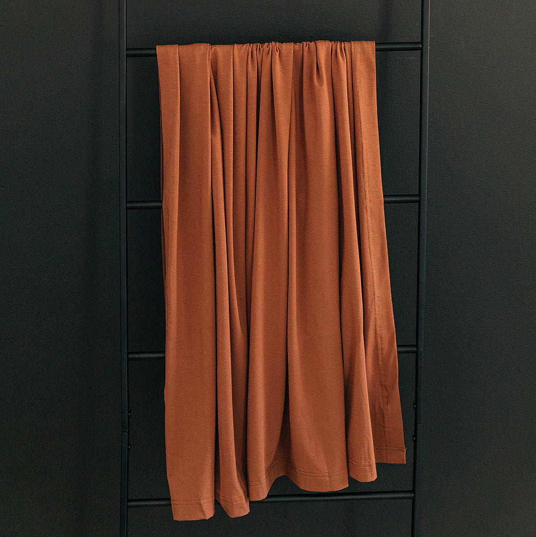 Brown curtain hanging on a black metal ladder against a dark wall