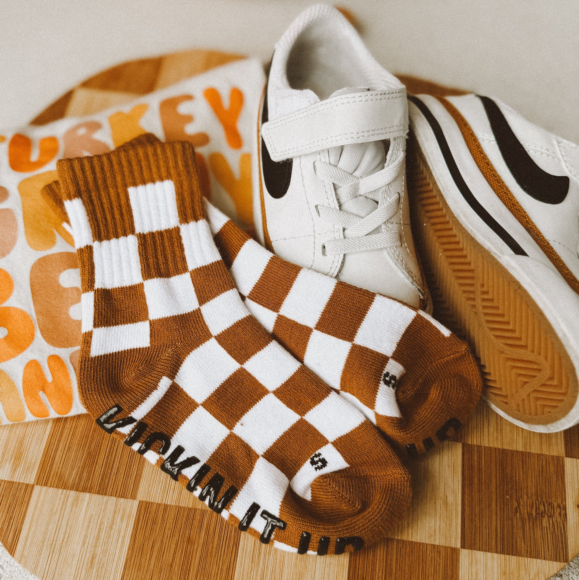 White sneakers with brown checkered socks on a wooden cutting board with a pumpkin in the background.