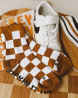 White sneakers with brown checkered socks on a wooden cutting board with a pumpkin in the background.