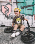 Child sitting on a balance bike in front of a graffiti-covered wall