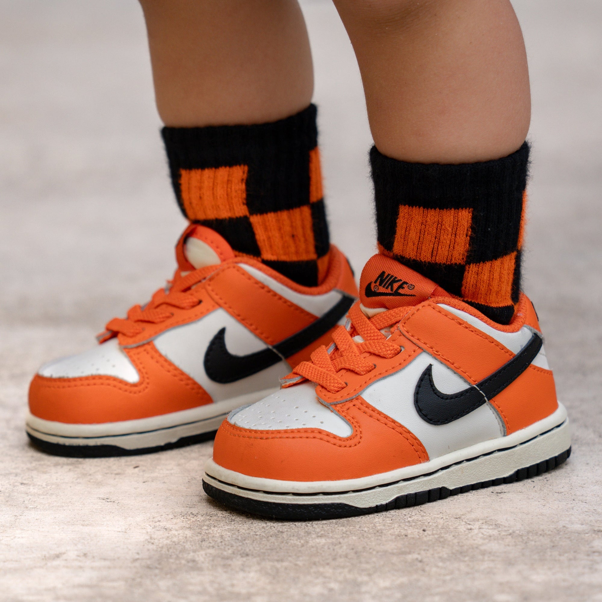 Orange sneakers with black Nike logo worn with orange and black checkered socks on a neutral background