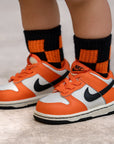 Orange sneakers with black Nike logo worn with orange and black checkered socks on a neutral background
