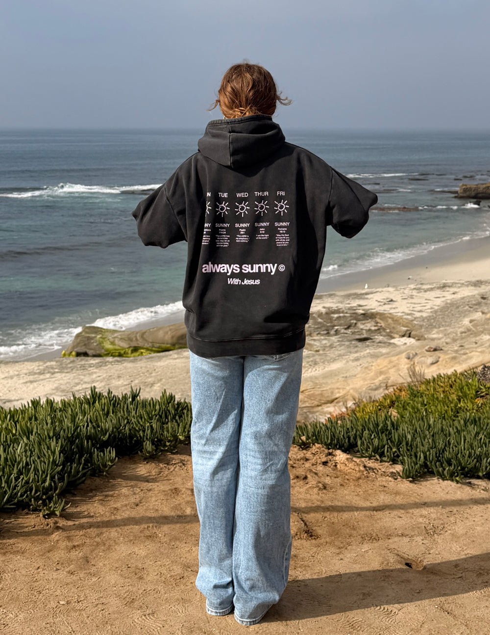 Black Christian hoodie with front pouch pocket, styled with jeans by the coast