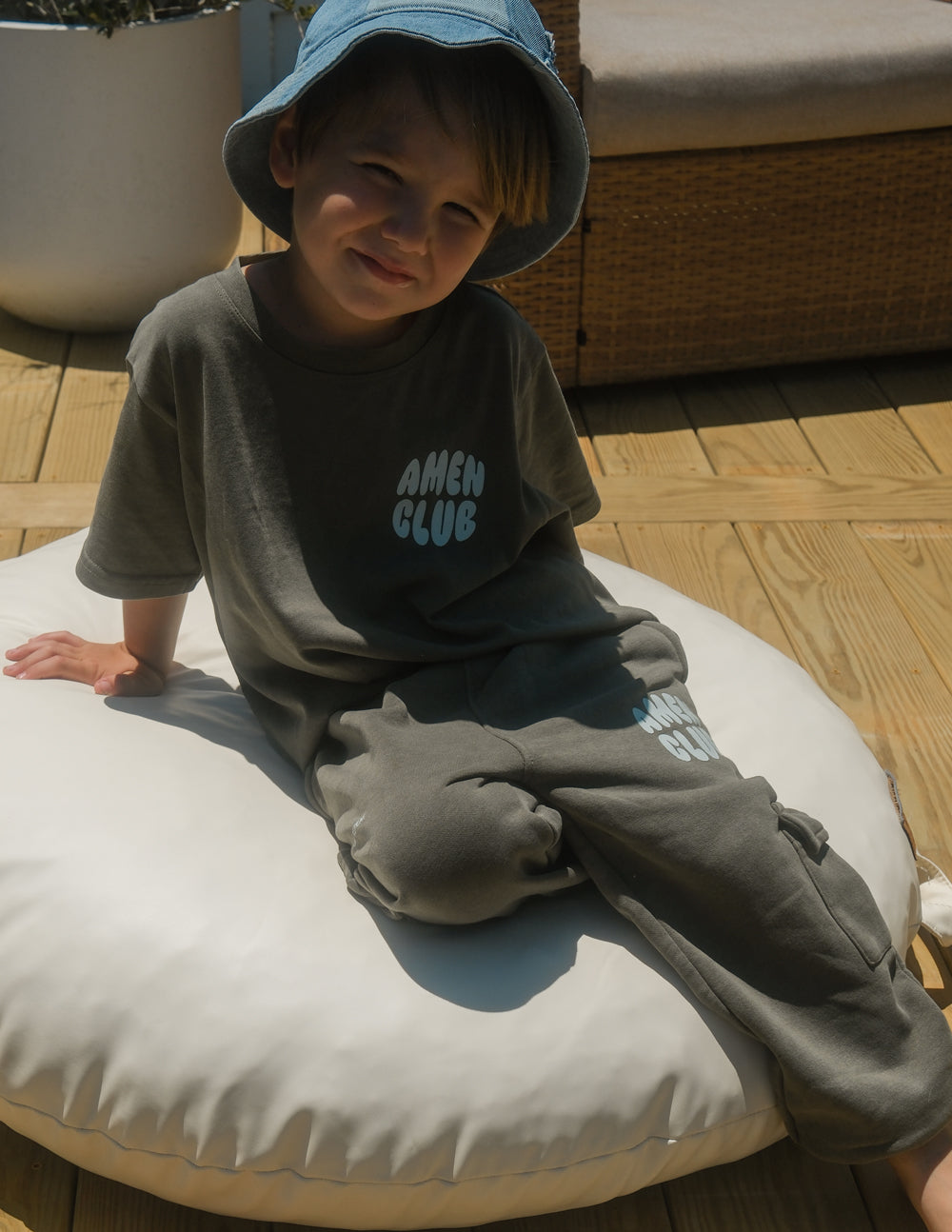 Child seated on a cushion wearing hunter green Amen Club cargo sweatpants