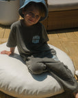 Child seated on a cushion wearing hunter green Amen Club cargo sweatpants