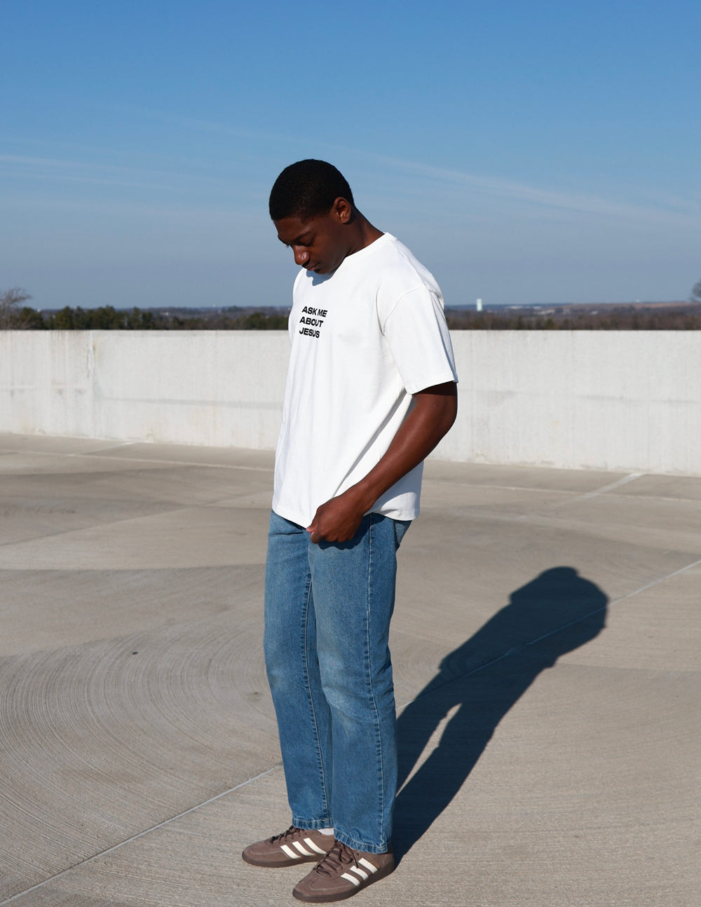 Full-length view of cream Ask Me About Jesus tee styled with blue jeans