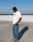 Full-length view of cream Ask Me About Jesus tee styled with blue jeans