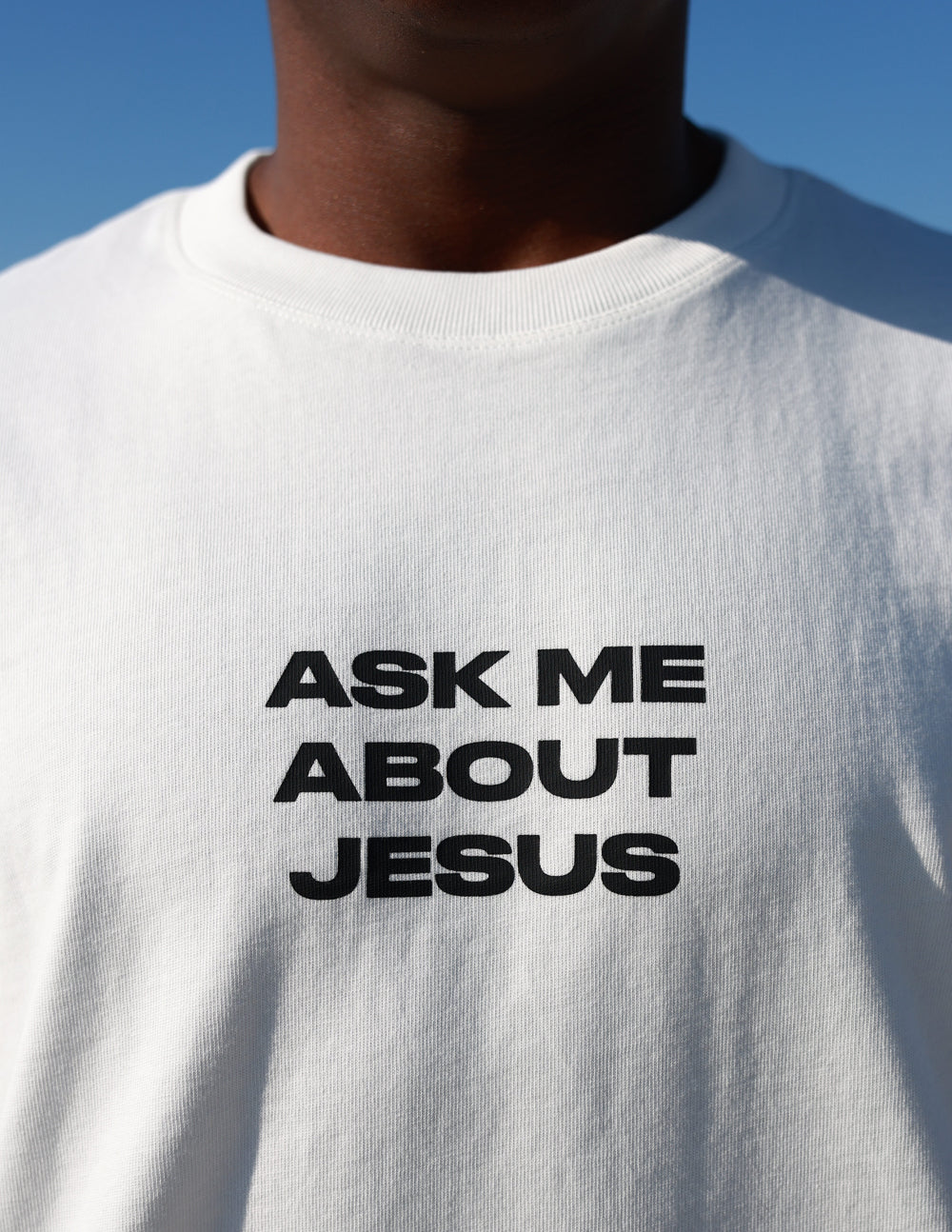 Close-up of bold black Ask Me About Jesus lettering on cream cotton tee