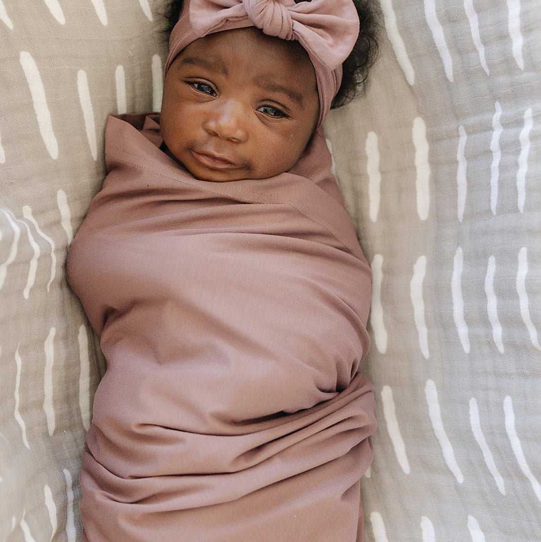 Newborn baby wrapped in a pink blanket with a matching headband on a beige and white patterned background