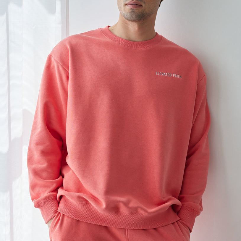 Man wearing a coral tracksuit with a logo against a white wall