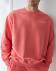 Man wearing a coral tracksuit with a logo against a white wall