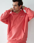 Man wearing a pink hoodie and pants with a brand logo on a white background