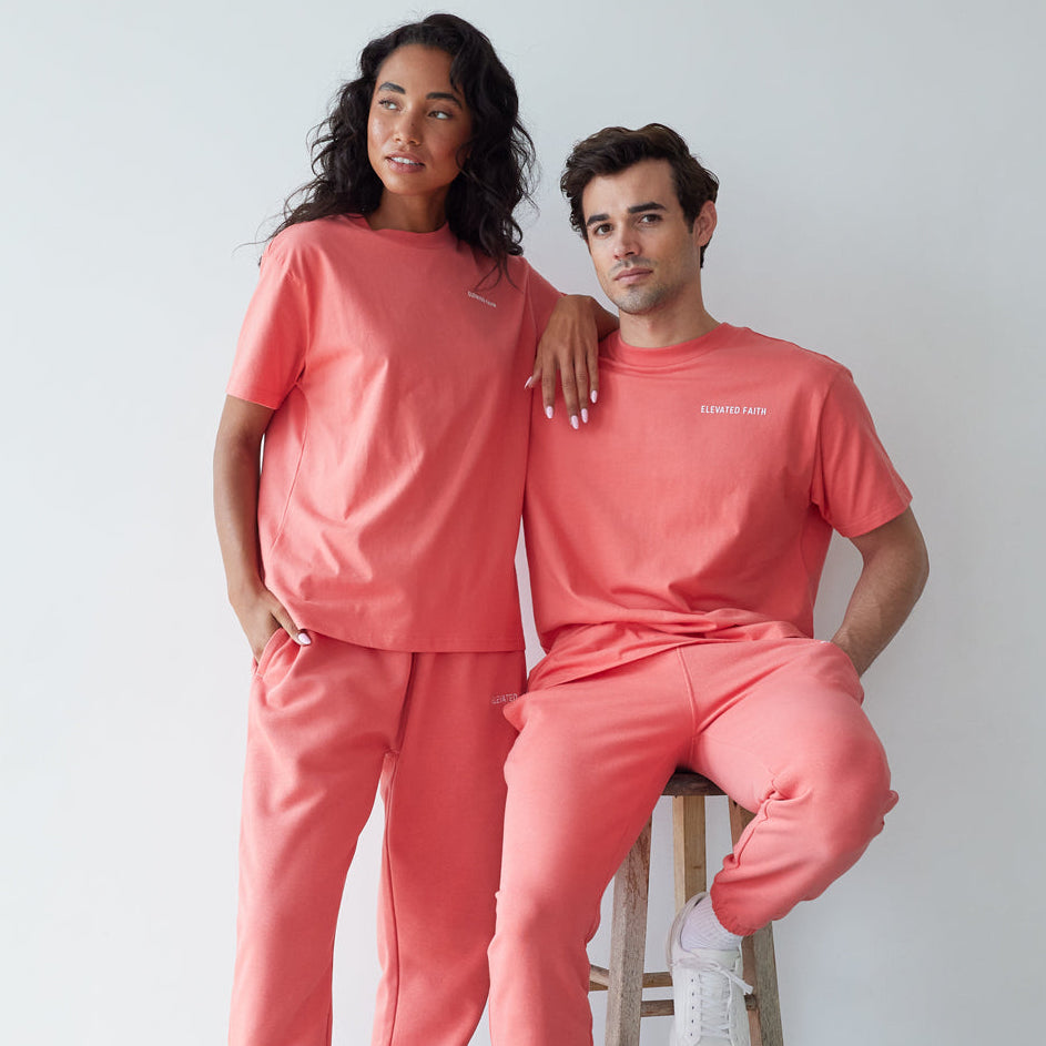 Two people wearing matching coral outfits with white sneakers against a plain background
