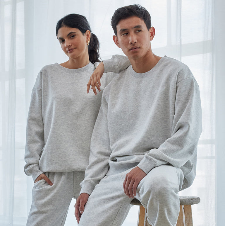 Two people wearing matching gray sweatshirt and pants sets in a minimalistic room.