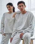 Two people wearing matching gray sweatshirt and pants sets in a minimalistic room.