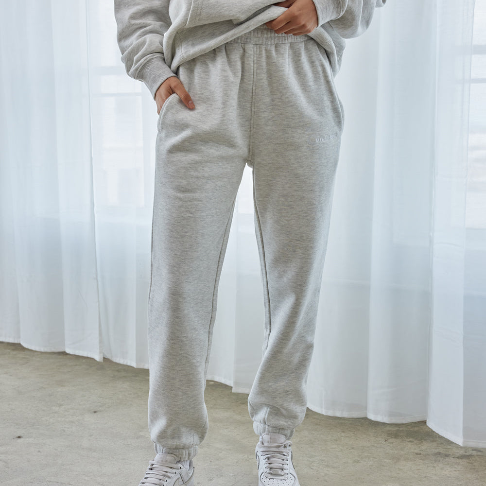 Person wearing a gray sweatshirt and pants with white sneakers in front of a white curtain.
