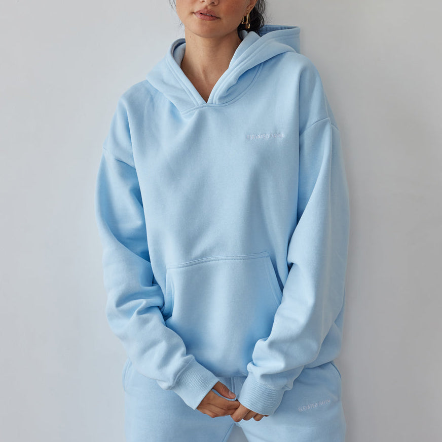 Woman wearing a light blue hoodie and pants against a plain background