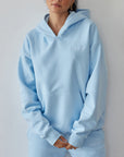 Woman wearing a light blue hoodie and pants against a plain background
