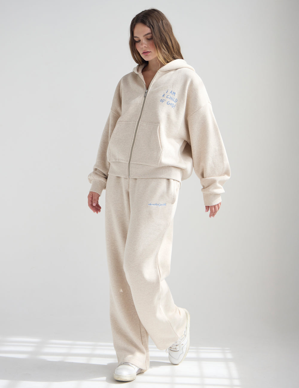 Woman wearing Heather Eggshell Basics wide leg sweatpants with a coordinating zip hoodie and light sneakers.