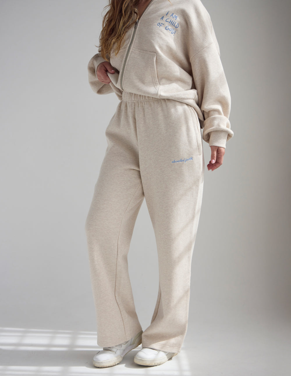 Angled view of a woman wearing Heather Eggshell wide leg sweatpants with a coordinating hoodie.